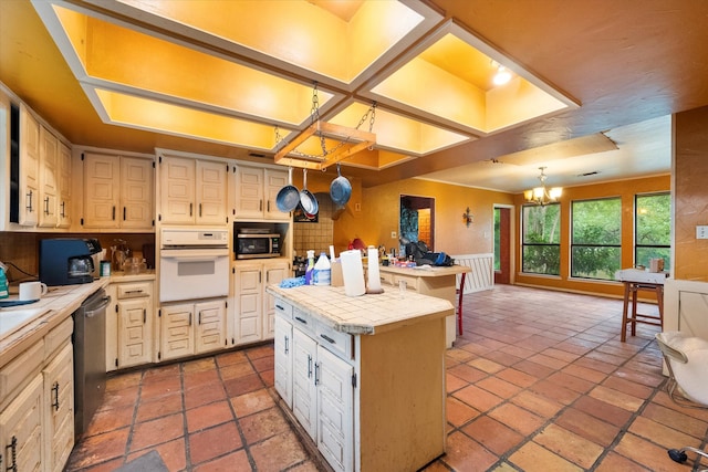 kitchen featuring tile countertops, stainless steel appliances, a kitchen island, an inviting chandelier, and hanging light fixtures