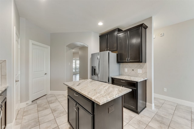 kitchen featuring light tile patterned floors, a center island, light stone countertops, stainless steel refrigerator with ice dispenser, and tasteful backsplash