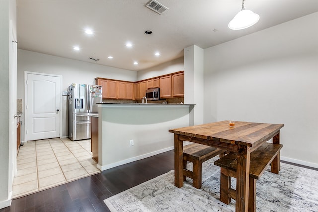 kitchen with appliances with stainless steel finishes, light hardwood / wood-style flooring, kitchen peninsula, and decorative light fixtures