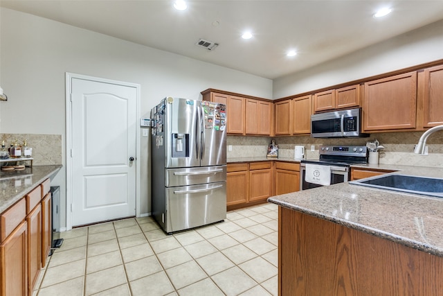 kitchen with stone countertops, light tile patterned floors, stainless steel appliances, sink, and decorative backsplash