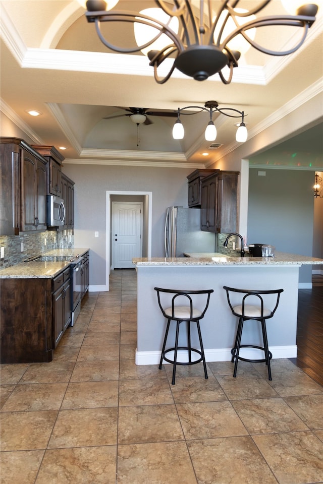 kitchen with a raised ceiling, ornamental molding, appliances with stainless steel finishes, and backsplash