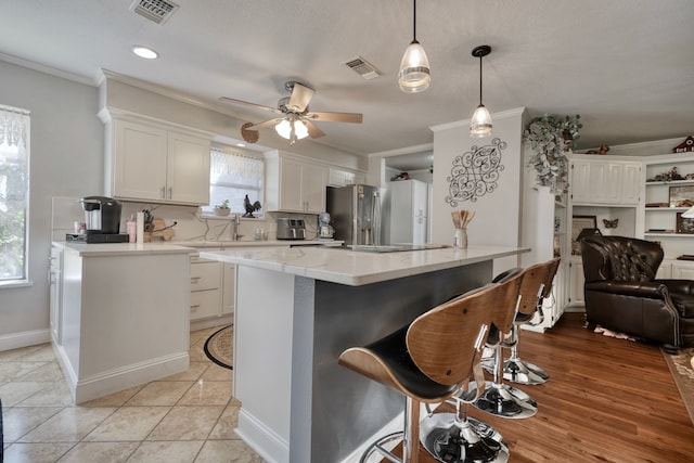 kitchen featuring white cabinets, a fireplace, decorative light fixtures, stainless steel fridge, and ceiling fan