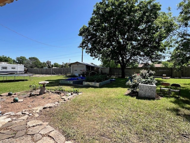 view of yard with a trampoline, a fenced backyard, a garage, an outdoor structure, and a vegetable garden