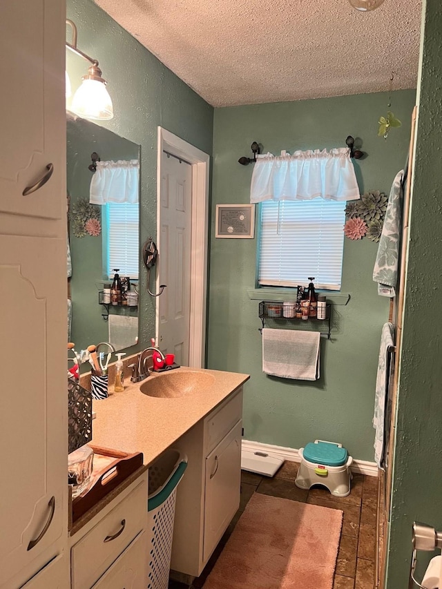 bathroom with vanity, baseboards, a textured ceiling, tile patterned floors, and a textured wall