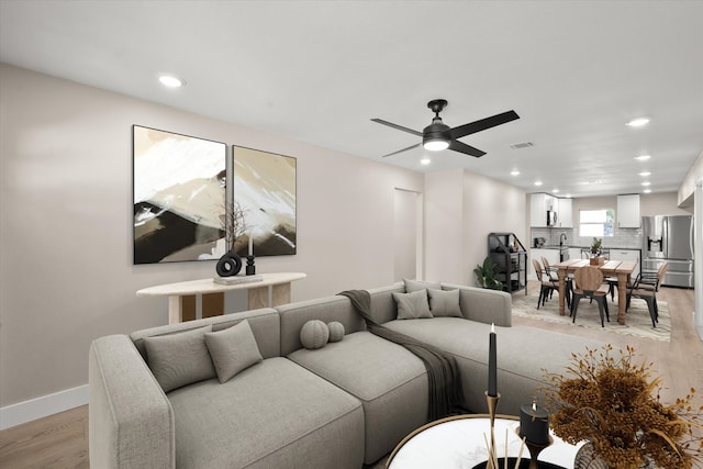 living room with light wood-type flooring, ceiling fan, and sink