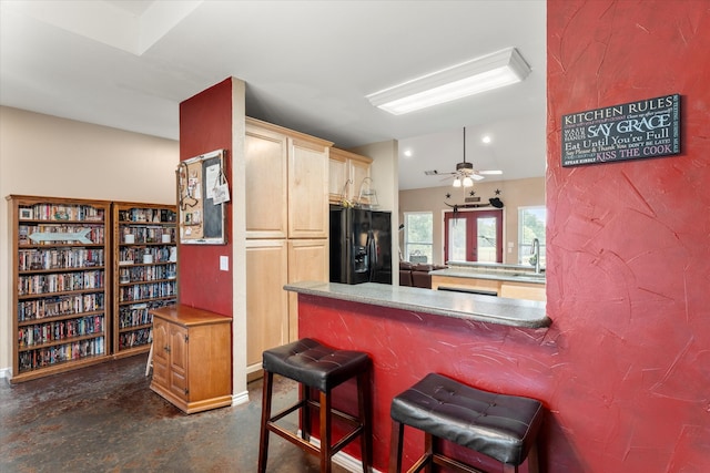 kitchen featuring sink, black fridge with ice dispenser, kitchen peninsula, ceiling fan, and a kitchen bar