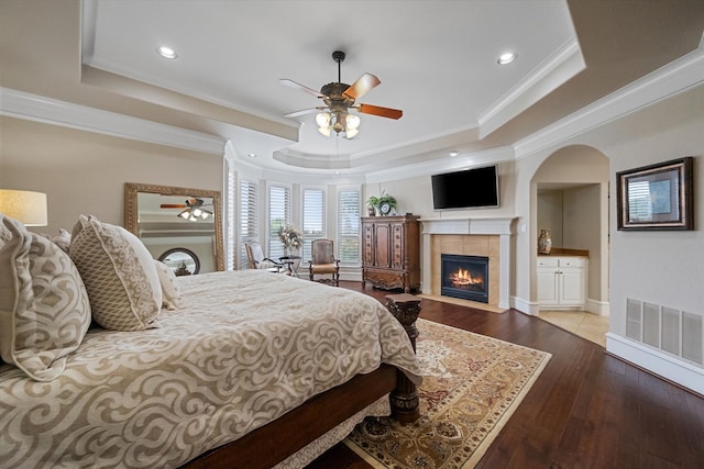 bedroom featuring light hardwood / wood-style flooring, a tray ceiling, and a tile fireplace