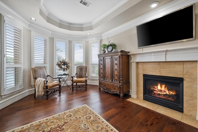 living area featuring a fireplace, wood finished floors, visible vents, ornamental molding, and a raised ceiling