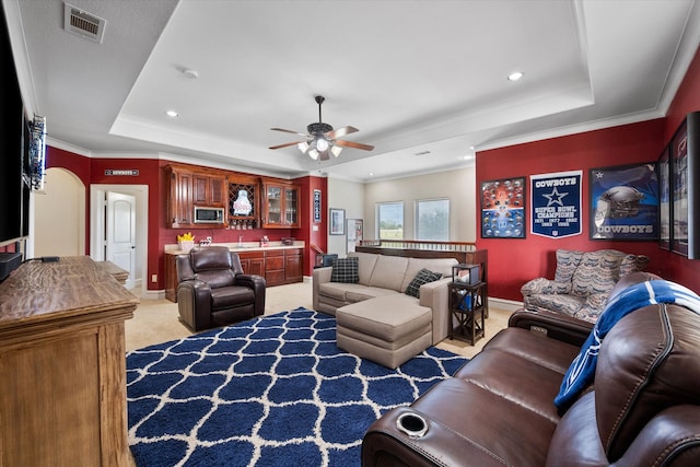 carpeted living room featuring ceiling fan, crown molding, a tray ceiling, and bar area