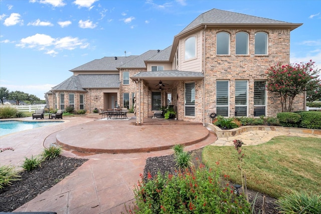 back of house with a ceiling fan, a patio area, an outdoor pool, and brick siding