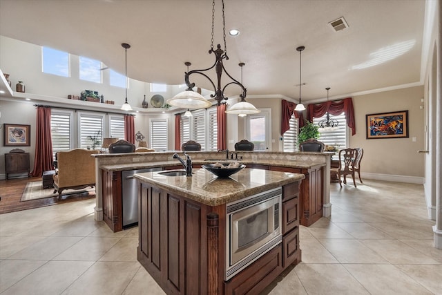 kitchen with stainless steel appliances, decorative light fixtures, an island with sink, and light tile patterned floors