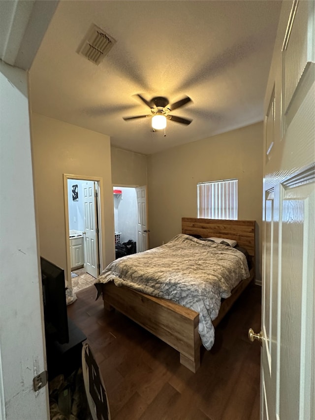 bedroom with a textured ceiling, dark hardwood / wood-style flooring, ceiling fan, and connected bathroom