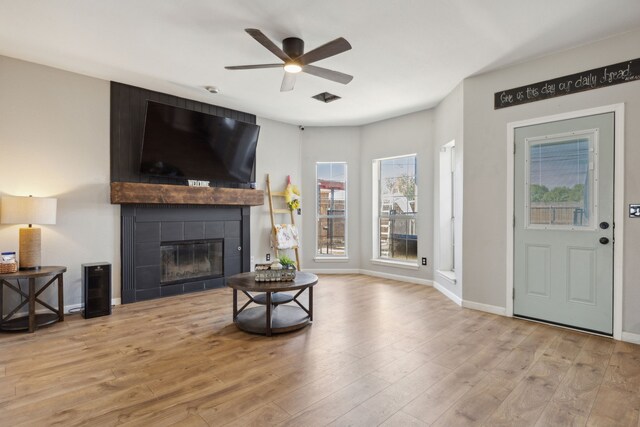 living room with ceiling fan, light wood-type flooring, and a tiled fireplace