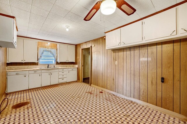 kitchen featuring white cabinets, ceiling fan, wooden walls, and sink