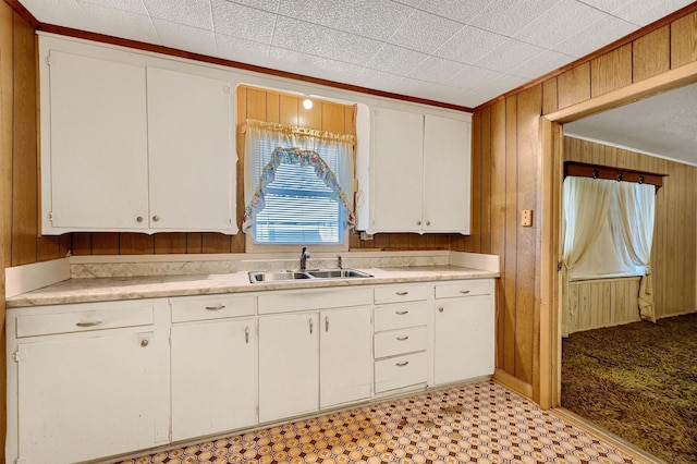 kitchen featuring crown molding, white cabinetry, sink, and wooden walls