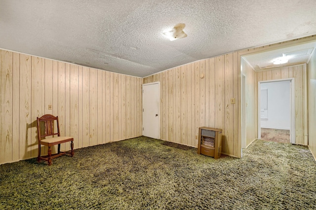 carpeted spare room featuring a textured ceiling, wood walls, and heating unit