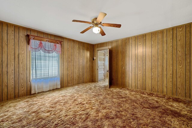 carpeted spare room with wood walls and ceiling fan