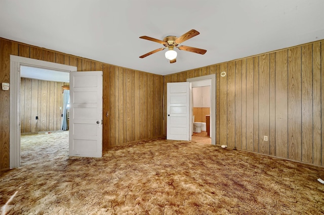 unfurnished bedroom with carpet flooring, ceiling fan, wooden walls, and ensuite bathroom