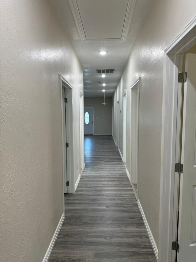 hallway featuring attic access, a textured wall, dark wood finished floors, baseboards, and visible vents