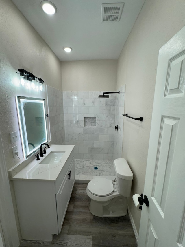 bathroom with tiled shower, vanity, toilet, and hardwood / wood-style flooring