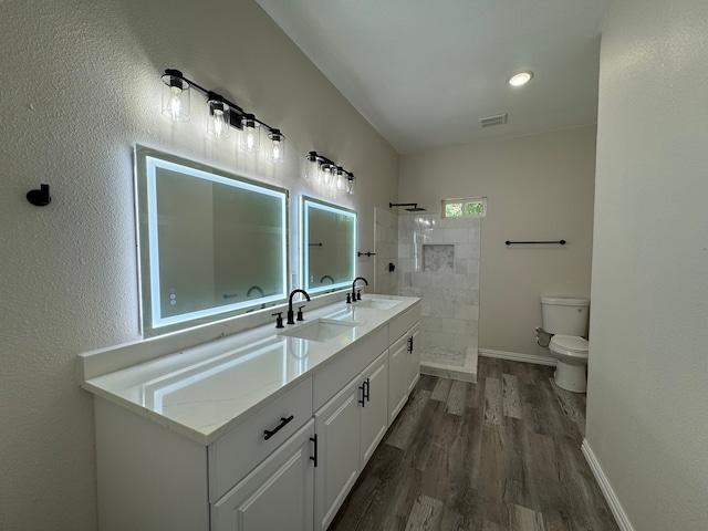 bathroom with a tile shower, vanity, toilet, and hardwood / wood-style flooring