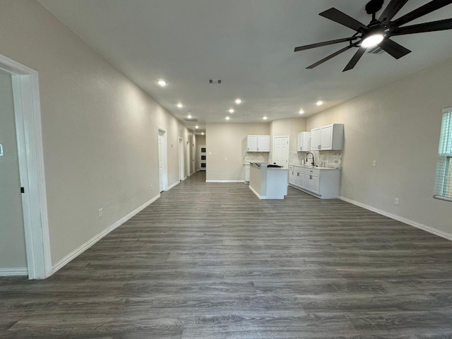 unfurnished living room with recessed lighting, dark wood-style floors, a ceiling fan, a sink, and baseboards