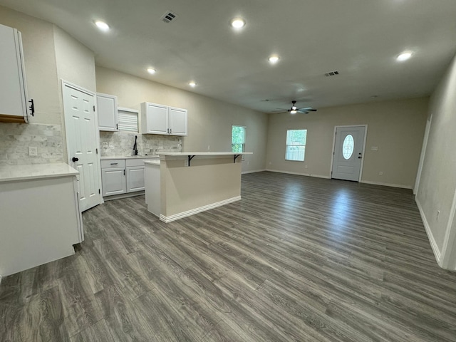 kitchen featuring ceiling fan, a kitchen island, white cabinetry, dark hardwood / wood-style floors, and a kitchen bar