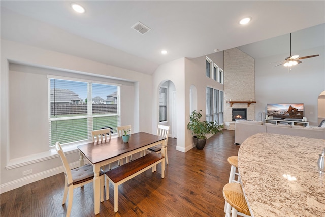 dining area with dark wood-type flooring, ceiling fan, vaulted ceiling, and a stone fireplace