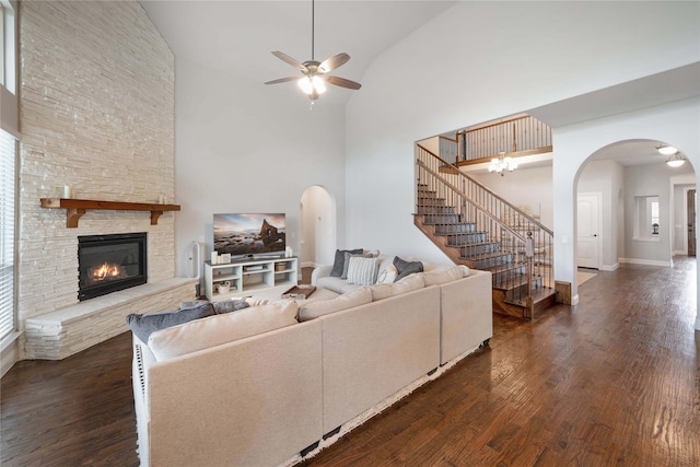 living room featuring dark hardwood / wood-style floors, high vaulted ceiling, ceiling fan, and a stone fireplace