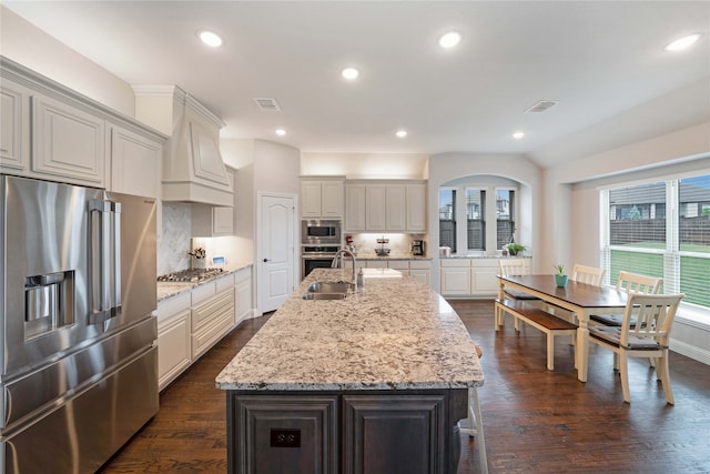 kitchen featuring appliances with stainless steel finishes, light stone counters, dark hardwood / wood-style floors, and an island with sink