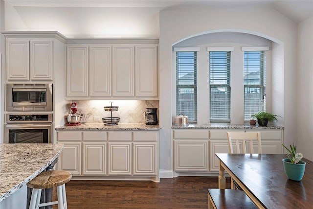 kitchen featuring vaulted ceiling, light stone countertops, dark hardwood / wood-style flooring, appliances with stainless steel finishes, and white cabinets