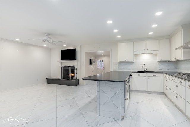 kitchen with dark countertops, a lit fireplace, backsplash, and a sink