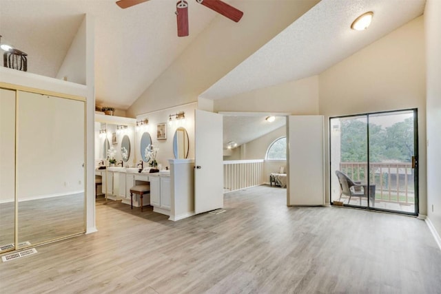 unfurnished living room with a textured ceiling, light wood-type flooring, high vaulted ceiling, and ceiling fan