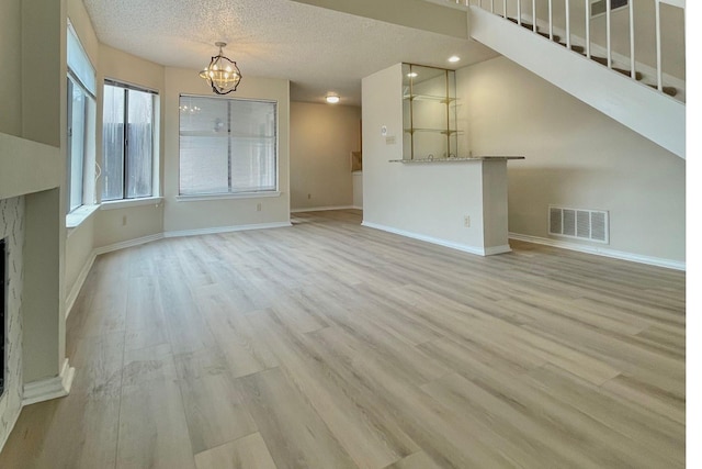 unfurnished living room with a chandelier, a textured ceiling, and light wood-type flooring