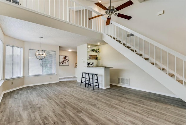 unfurnished living room featuring a textured ceiling, hardwood / wood-style floors, a towering ceiling, and ceiling fan with notable chandelier