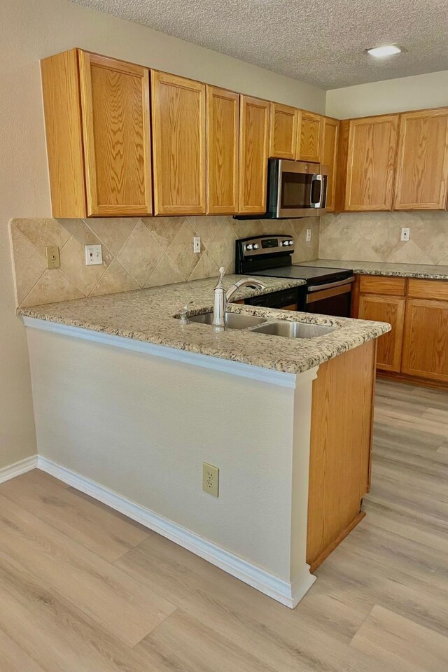 kitchen with sink, a textured ceiling, appliances with stainless steel finishes, and light hardwood / wood-style flooring