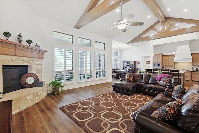 living room featuring hardwood / wood-style flooring, beam ceiling, high vaulted ceiling, a stone fireplace, and ceiling fan