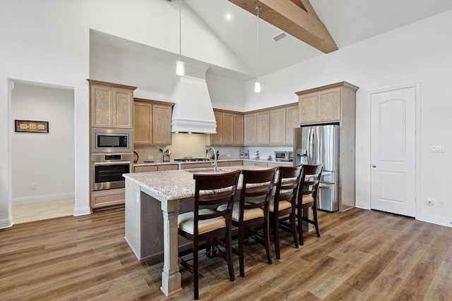 kitchen with dark wood-type flooring, a kitchen island with sink, custom exhaust hood, high vaulted ceiling, and appliances with stainless steel finishes