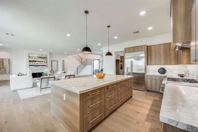 kitchen featuring pendant lighting, a spacious island, decorative backsplash, light stone counters, and stainless steel appliances