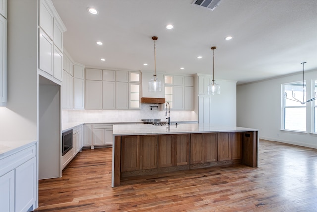 kitchen featuring decorative backsplash, white cabinets, pendant lighting, a center island with sink, and hardwood / wood-style floors