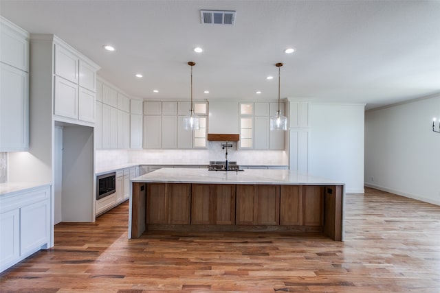 kitchen with light hardwood / wood-style floors, hanging light fixtures, a large island with sink, and white cabinetry