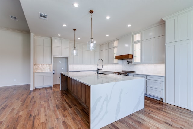 kitchen with a large island, white cabinets, wood-type flooring, and light stone countertops