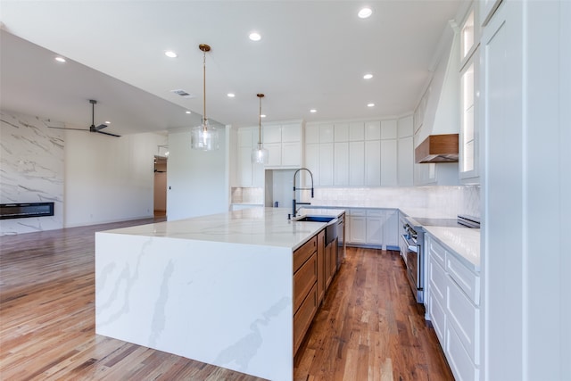 kitchen with light stone counters, white cabinets, a large island with sink, and light hardwood / wood-style floors