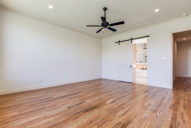 unfurnished bedroom featuring ornamental molding, light wood-type flooring, ceiling fan, and a barn door