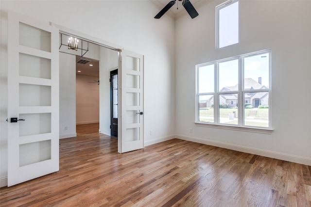 unfurnished room with ceiling fan with notable chandelier, wood-type flooring, a towering ceiling, and built in shelves