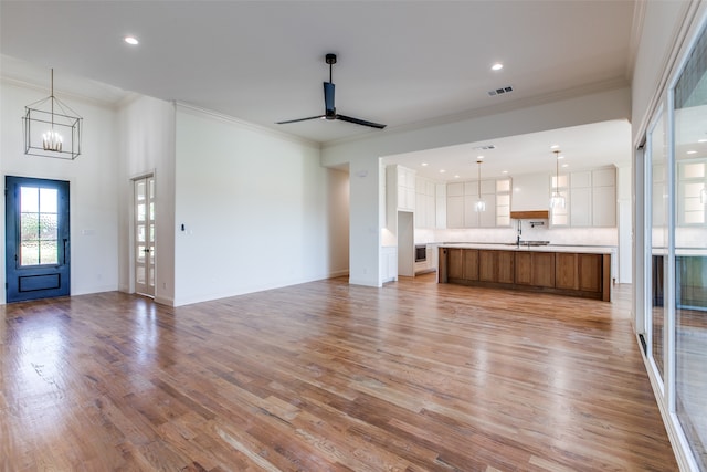 unfurnished living room with ceiling fan with notable chandelier, light wood-type flooring, and ornamental molding