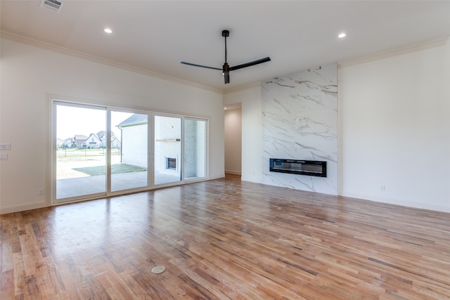 unfurnished living room featuring ceiling fan, light wood-type flooring, a premium fireplace, and ornamental molding