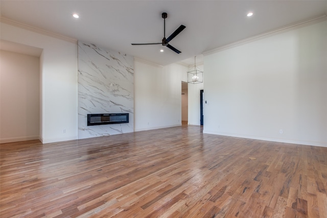 unfurnished living room with ceiling fan with notable chandelier, light wood-type flooring, a premium fireplace, and ornamental molding