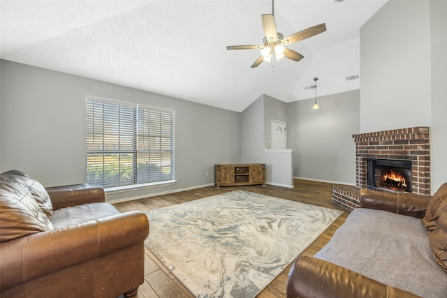 living room featuring light wood-type flooring, a brick fireplace, a textured ceiling, vaulted ceiling, and ceiling fan