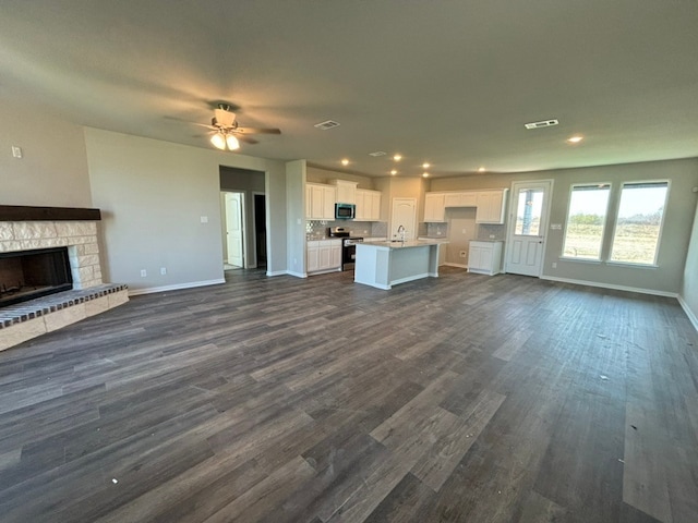 unfurnished living room with a fireplace, ceiling fan, dark wood-type flooring, and sink